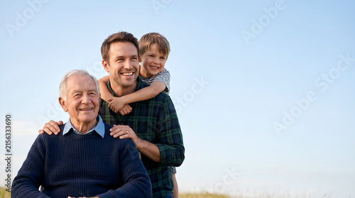 Three generations of happy men smiling together outdoors against a blue sky, representing family bonds