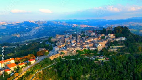 Stunning aerial pullback truck right pan left pedestal up shot from Santa Vittoria in Matenano, the high promontory full of thickets and trees where the town centre lies with its historic buildings