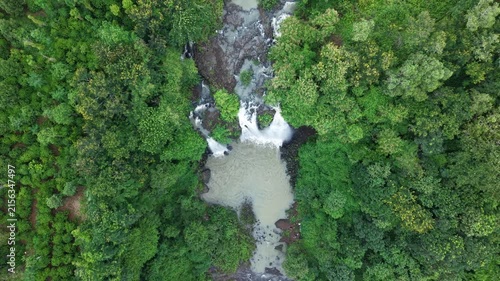 Cinematic top-down drone footage looking directly down at a spectacular three-stream waterfall as the camera gradually ascends. The widening aerial perspective progressively reveals the waterfall