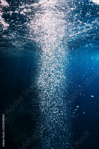 фотографія Bubbles rising to the water surface in blue ocean with sunlight.