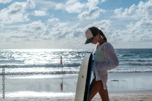 Foto Skater girl in profile holding bodyboard on sunny beach