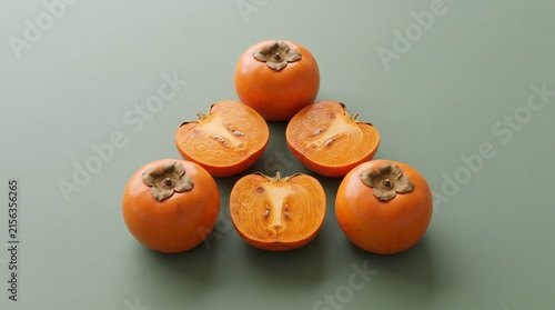 Persimmons Arranged in a Pyramid on a Green Background. Fresh Orange Fruit, Sliced and Whole, with Textured Skin and Seeds.