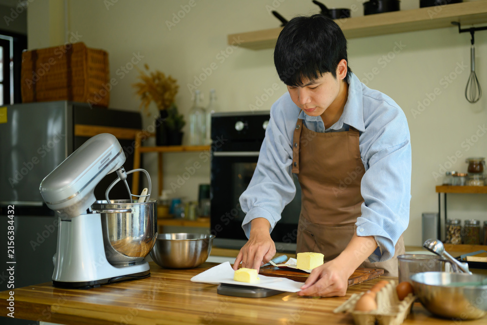 Fototapeta premium Young Asian Man Preparing Butter for Cookie Making Process in Modern Home Kitchen