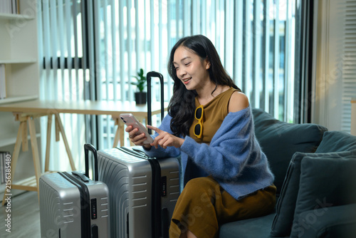Young Woman Using Smartphone Beside Luggage Suitcases Before Trip, Travel Planning at Home