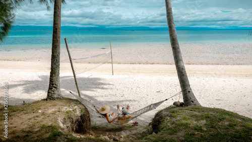 Top view of couple tourist are in motion of relaxing stay under coconut palm tree at the the edge of the sea beach,  trip summer on vacation of couple lover
