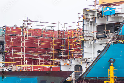 Industrial shipbuilding operation showing large hull and superstructure sections under assembly, with extensive temporary scaffolding and safety installations.