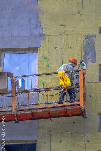 A construction worker is finishing the facade on a summer day