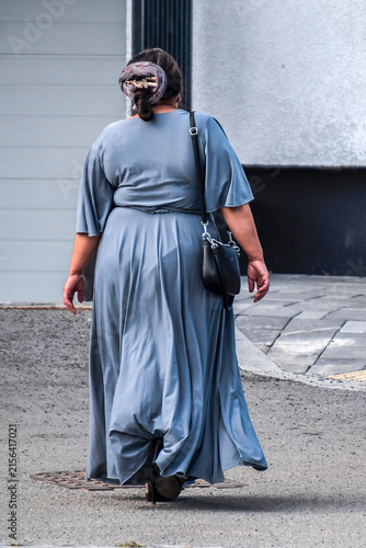 Gypsy woman with a shoulder bag walks along the sidewalk on a summer day