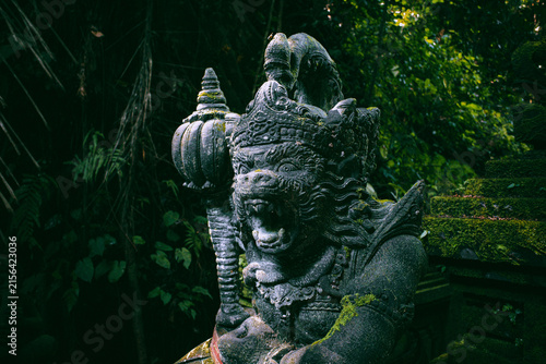 Balinese Hanuman guardian statue, a revered Hindu deity figure carved from stone, protecting a temple entrance surrounded by lush green jungle foliage in Bali, Indonesia