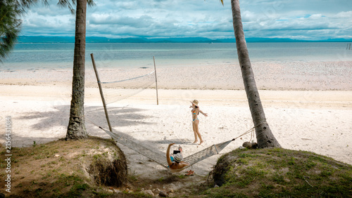 Top view of couple tourist are in motion of relaxing stay under coconut palm tree at the the edge of the sea beach,  trip summer on vacation of couple lover