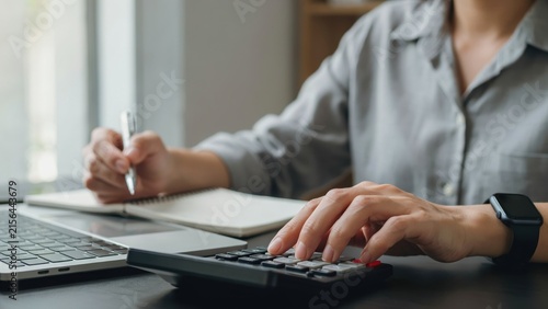 A person sitting at a desk using a calculator and writing in a notebook next to a laptop, focusing on financial planning and accounting
