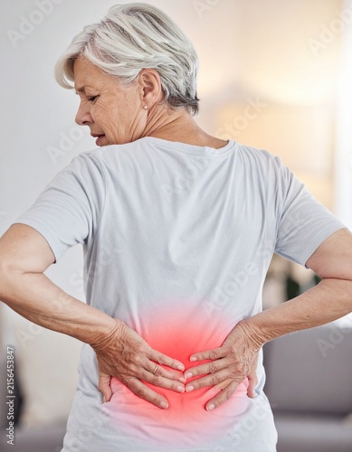 Senior woman holding her lower back due to severe spinal pain and inflammation indoors.