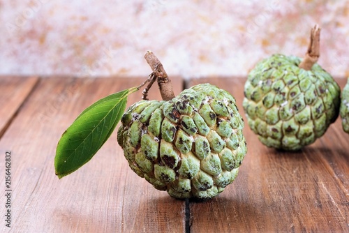 Fotografía Ripe atemoya custard apple fruits displayed with green leaves on a rustic surface, showing their distinctive segmented texture and natural tropical appearance