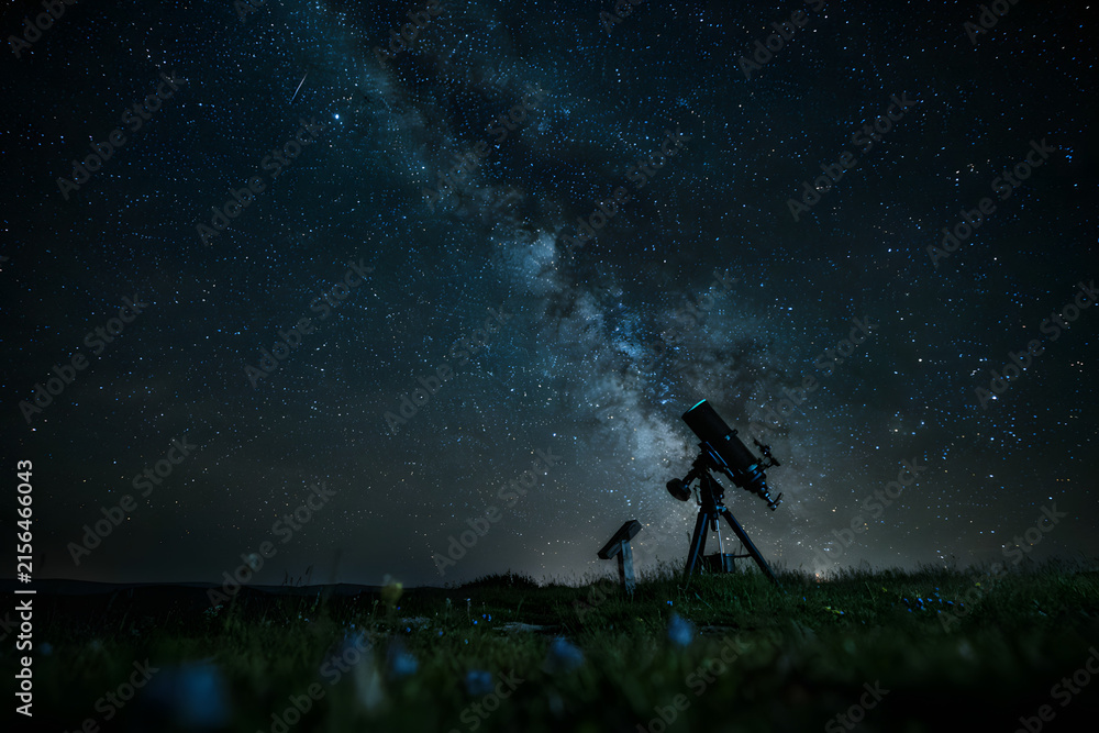 Fototapeta premium Silhouette of an astronomical telescope positioned on a dark grassy hill under a vast night sky with the glowing milky way galaxy visible