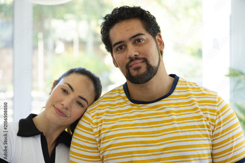 Fototapeta premium Diverse couple standing close in bright room by windows, wearing striped T-shirt and collared top