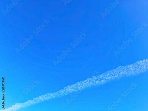 Clear Blue Sky Background with White Airplane Contrail and Subtle Crescent Moon Daytime View