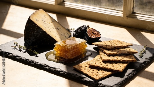 Dark aged cheese wedge, honeycomb, figs, and crackers on slate board