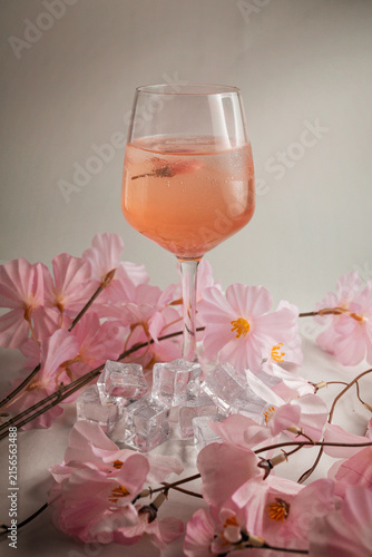 Pink spring cocktail with ice cubes and cherry blossom flowers on light background with copy space