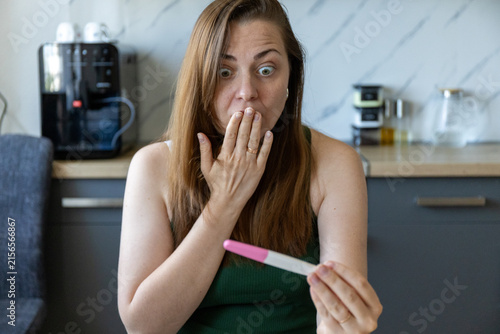 Konstfotografi Shocked young woman looking at positive pregnancy test at home