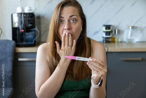 Bild auf Leinwand Shocked young woman looking at positive pregnancy test at home