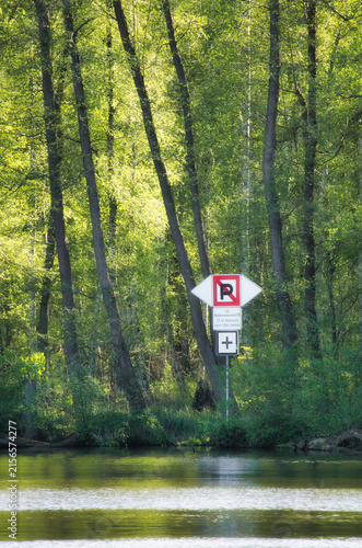 A Traffic Sign Near a Forest Riverbank Surrounded by Lush Green Trees - Nature