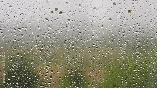 Raindrops falling down a window pane during a storm Heavy rain on glass surface with blurry green nature background video FullHD