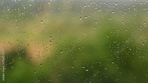 Raindrops falling down a window pane during a storm Heavy rain on glass surface with blurry green video FullHD nature background