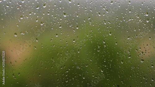Raindrops falling down a window pane during a storm Heavy rain on glass surface with blurry green FullHD nature background video