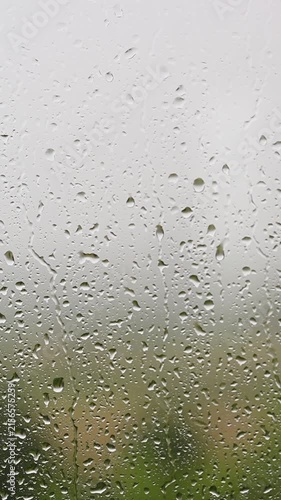 Raindrops falling down a window pane during a storm Heavy rain on glass surface with blurry green nature vertical video FullHD background