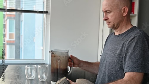 Bald man pouring a healthy protein shake from a blender into two glasses at home for a nutritious breakfast