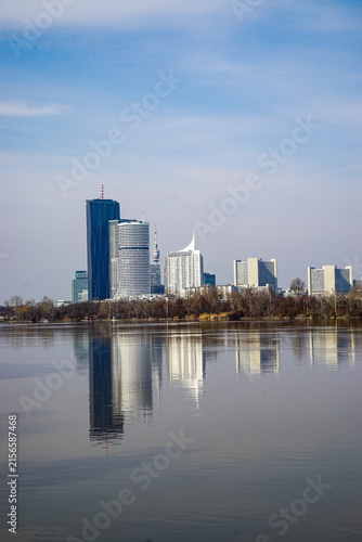 A contemporary urban skyline rises beyond a calm river, with modern architecture and clear reflections creating a spacious cityscape suitable for travel and business imagery.