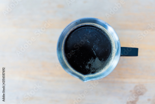 Hot espresso shot into a stainless cup placed on wooden table in a coffee shop.