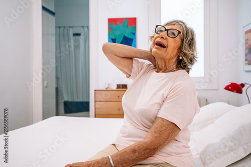 Senior woman feeling neck pain and discomfort in bedroom