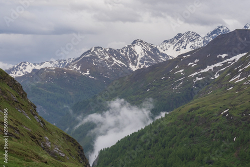 Fotografie Picturesque Grossglockner High Alpine Road in Austria surrounded by rugged snowy peaks, green Alpine slopes and dramatic cloudy mountain scenery