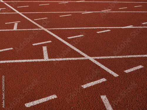 Obraz na płótnie Textured red rubber running track surface featuring solid white lane lines contrasted with smaller blue and yellow markings