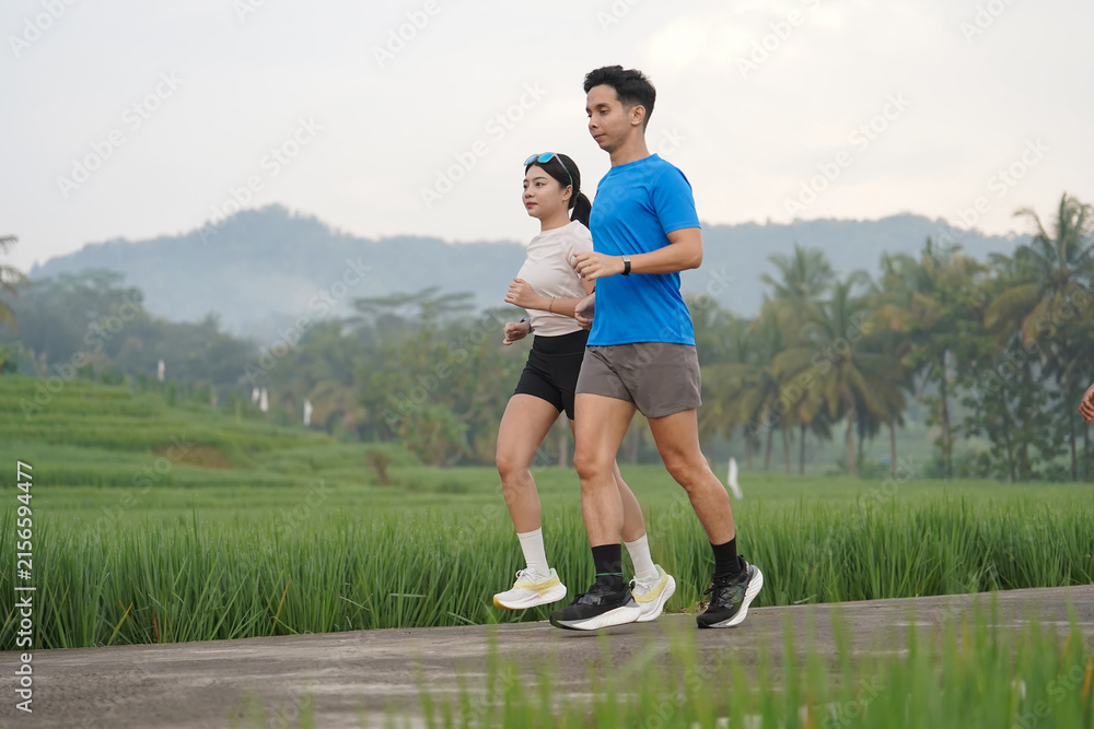 Obraz premium Asian Indonesian Couple Jogging Beside Rice Fields and Tropical Mountain Landscape in Yogyakarta