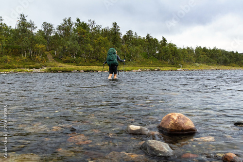 Fotografía Backpacker wading river water current with rocks in Sweden