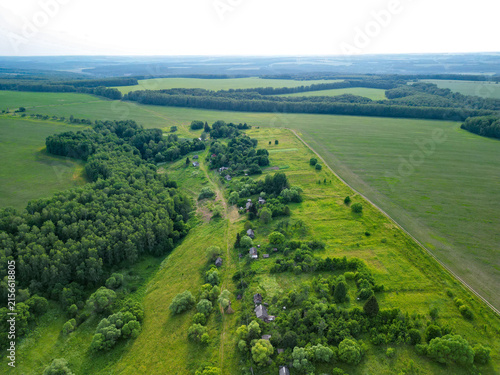 Abandoned village surrounded by dense forest. Atmospheric rural landscape featuring deserted houses, overgrown vegetation, and signs of a forgotten settlement.