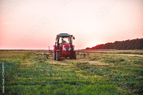 Modern red tractor working with forage harvesting equipment in an agricultural field. Contemporary farm machinery used for efficient hay and forage production.