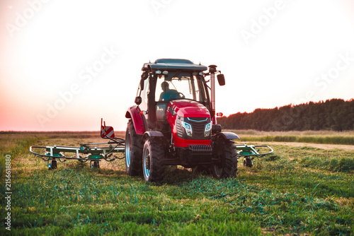 Obraz na płótnie Modern red tractor working with forage harvesting equipment in an agricultural field