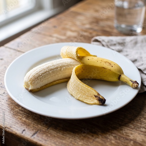 Partially peeled yellow banana on a white plate on a rustic wooden table