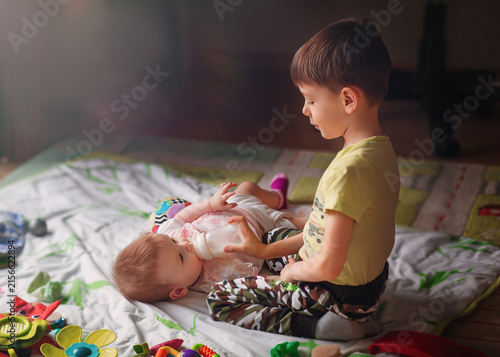 Fotografía Boy bottle-feeds his baby sibling on a bed at home, offering gentle care in a cozy bedroom