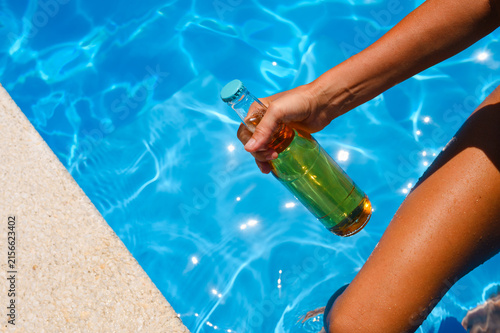 A woman with a bottle of beer enters a hotel pool. A cold drink on a summer day.