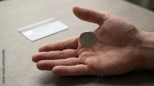 Hand Holding Coin Above Blank Payment Card on Soft Neutral Background