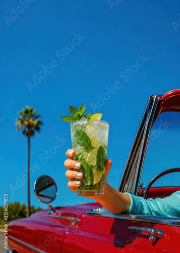 Refreshing mojito cocktail held from red vintage convertible on sunny summer day