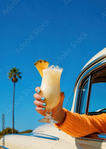Tropical pineapple cocktail held from vintage car on sunny summer day