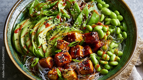 Healthy vegan poke bowl with tofu, avocado, edamame, and glass noodles in a ceramic bowl, top view