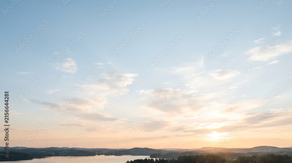 Obraz premium Panoramic view of a serene lake surrounded by dark forests under a vast sky with soft clouds during sunrise or sunset.