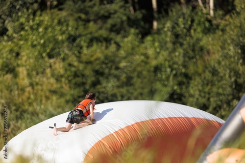 Konstfotografi A child joyfully climbs atop a colorful inflatable water trampoline, excitement