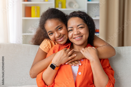 Obraz na plátne Happy Black mother and young daughter embracing on sofa at home and smile at cam
